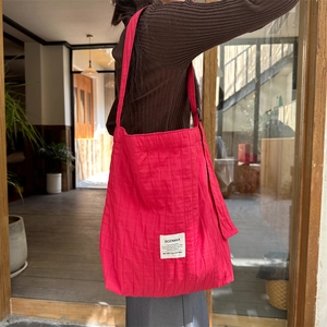 Detail of rose red pleated canvas tote bag worn by model in a street style setting
