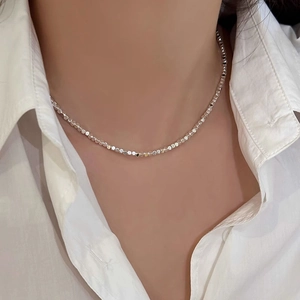 Gros plan d'un collier minimaliste en perles cubiques argentées sur une chemise