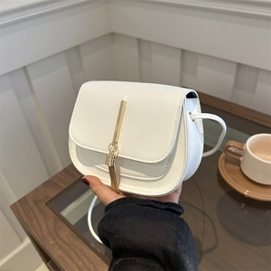Minimalist white faux leather saddle bag with gold tassel fringe held in a cafe setting