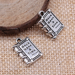 Antique silver book-shaped charms engraved with Once Upon A Time on wooden background