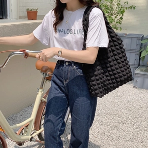 Outdoor shot of a large black bubble-textured shoulder tote bag on a model