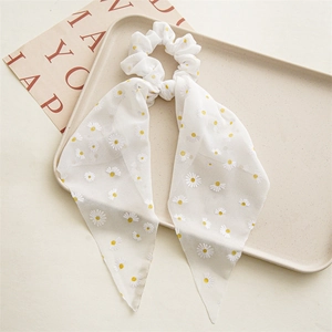 Detail of white chiffon hair scrunchie with daisy prints and long ribbons on a tray