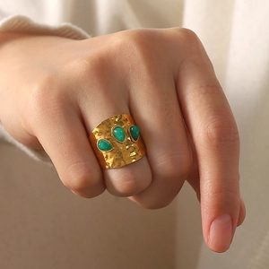 Detailed view of wide gold hammered ring with three green teardrop stones on a finger
