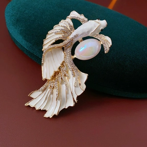 Macro shot of gold fish brooch with white enamel fins and a large opal gemstone