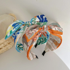 Close-up of wide satin headband with vibrant abstract floral prints and a large bow design