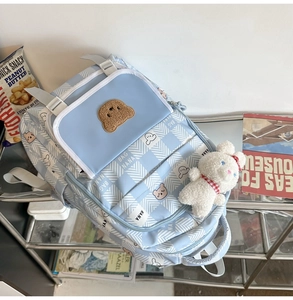 Detail of light blue plaid school backpack featuring a cute bear pattern and plush charm