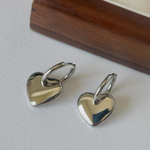 Detailed close-up of polished heart-shaped pendant earrings in a mirror-like silver finish