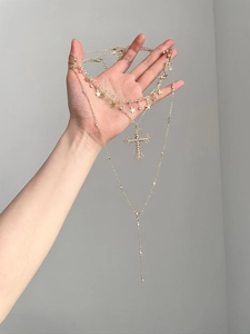 Detail of three-layer gold necklace featuring cross pendant and star charm with crystals