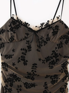Détail du tissu en maille nude avec broderie florale noire et petit nœud sur la robe