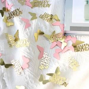 Macro detail of gold Happy Birthday confetti and pink butterfly sequins on fabric