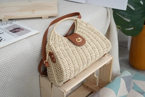 Detail of woven straw bag with brown leather flap, golden metal buckle and top handle