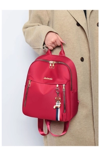 Detail of red water-resistant nylon backpack with golden zippers and a cute bear pendant