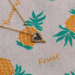 Close-up of heart pendant with rainbow stones on gold chain over fruit pattern cloth
