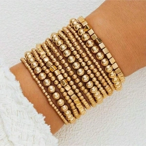 Detail of layered gold beaded bracelets with round and square beads on a model's wrist