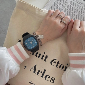 Close-up of square black watch with blue dial, silver chain bracelet and rings on canvas