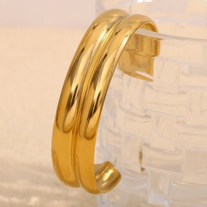 Dettaglio del bracciale rigido doppio strato placcato oro 18K appeso sul bordo di un vetro