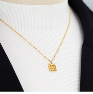 Detail of a square grid chocolate pendant on a gold asymmetric chain worn on a black blazer