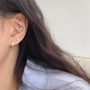 Detail of square zircon silver hoop and minimalist pearl stud earrings worn on ear