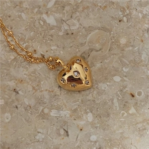Macro detail of a 3D gold heart pendant with zircon star settings on a beaded chain