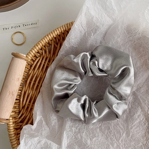 Close-up of silver satin scrunchie with pleated texture on white paper background