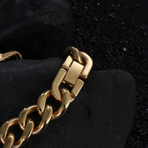 Macro detail of a gold Cuban link chain bracelet featuring a secure fold-over clasp