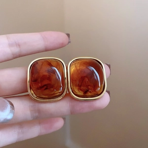 Close-up of amber resin earrings with gold edges held in hand, vintage style detail