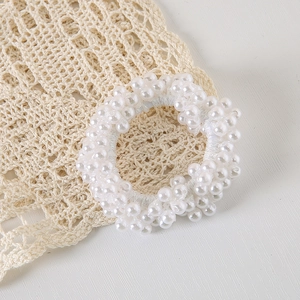 Detail of white pearl elastic hair tie placed on minimalist lace background