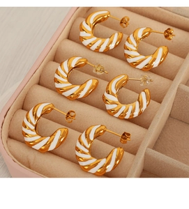 Detailed view of three pairs of gold and white enamel striped C-shape earrings in a pink box
