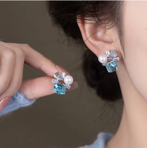 Detailed view of silver post square blue crystal and pearl stud earrings worn by a model