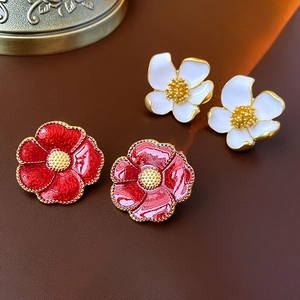 Close-up of vintage metal flower earrings in red and white enamel with golden edges