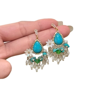 Vintage style floral drop earrings with turquoise tassels and pearls in a hand-held view