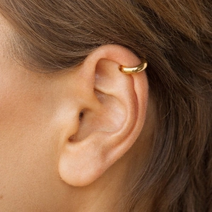 Close-up of polished gold C-shape ear cuff earring worn on a female model's ear