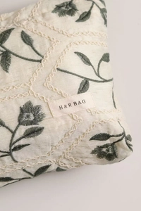 Close-up of floral embroidery and woven label on a cream cotton linen cosmetic bag