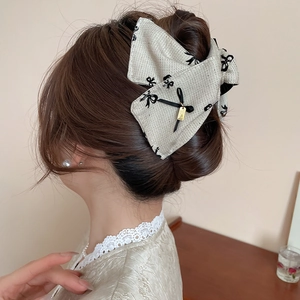 Detailed view of beige tweed bow hair claw clip with golden pendant in hair styling