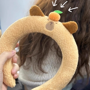 Detailed plush capybara headband with a cute orange decoration on soft brown faux fur