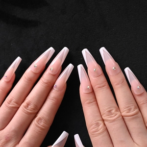 Close-up of nude pink coffin press-on nails with white V-cut tips and sparkling rhinestones