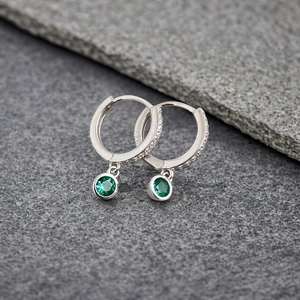 Macro detail of S925 silver hoop earrings with micro-set zircon and green gems