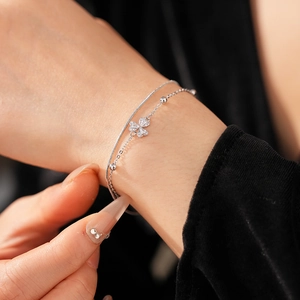 Detailansicht eines zweilagigen Silberarmbands mit Kleeblatt-Anhänger am Handgelenk