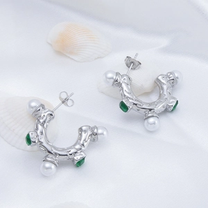 Detailed shot of silver C-shaped earrings with pearls and green gemstones on white fabric