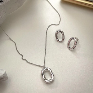 Macro detail of irregular silver geometric earring and necklace set on a textured surface