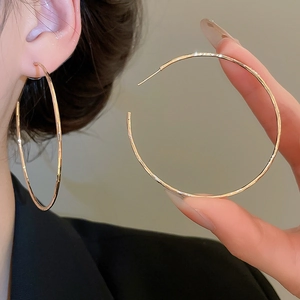 Détail de grandes boucles d'oreilles créoles dorées portées avec un éclat métallique