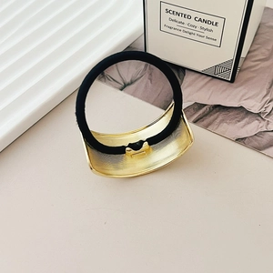 Close-up of golden textured metal hair tie with high-elastic black cord on a chic table