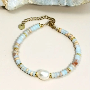 Detail of beaded bracelet with blue stones and a large baroque pearl on a beige surface