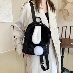 Fashionable black and white bunny ear plush backpack shown on a model in a cozy cafe setting