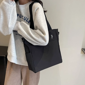 Minimalist large black canvas tote bag with front zipper pocket shown on model