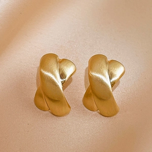 Macro shot of matte gold X-shaped cross earrings with brushed metal texture on silk