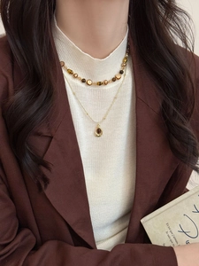 Détail d'un collier rétro double couche en œil de tigre sur un pull en maille blanc