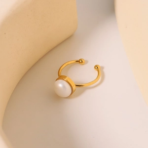 Elegant gold titanium steel ring with natural freshwater pearl on soft beige backdrop