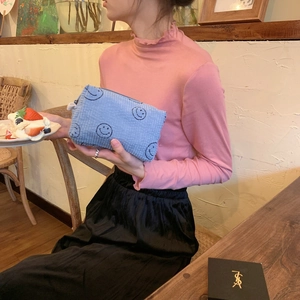 Corduroy makeup bag with smiley pattern held by a model in a cozy cafe setting