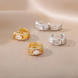 Detail of gold and silver C-shaped hoop earrings with zircon on champagne silk fabric